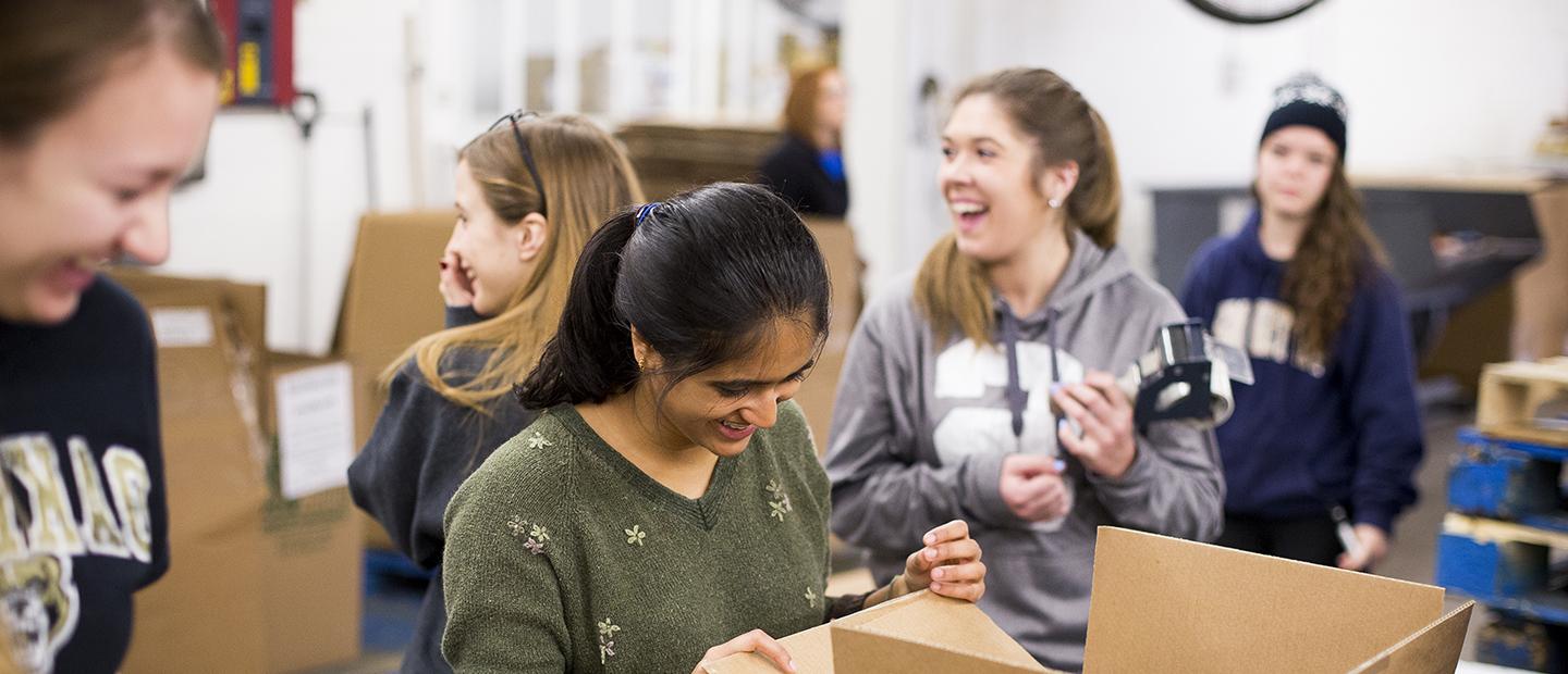 image of five women in a warehouse who are laughing and packing boxes