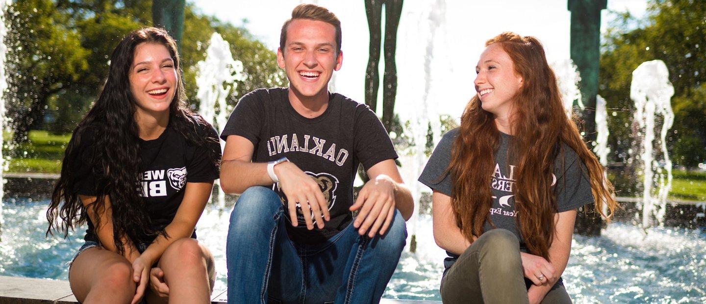 三个365英国上市官网的学生坐在喷泉边，笑个不停.