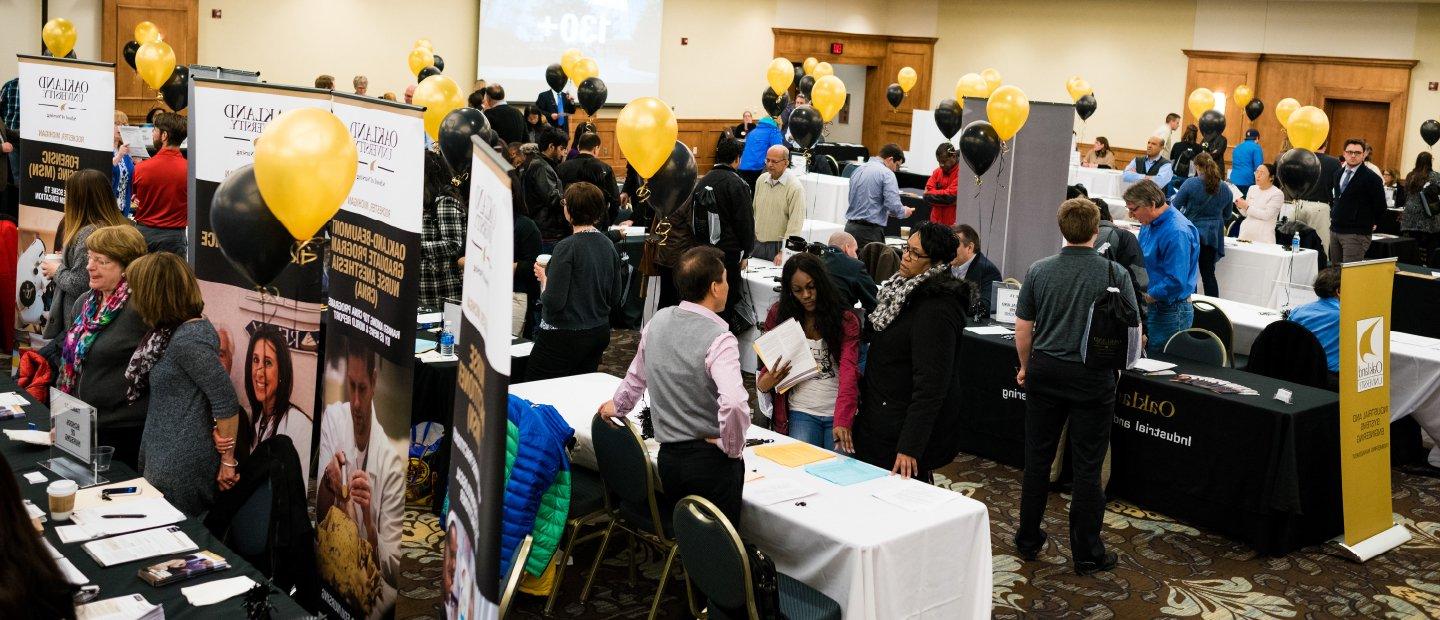 Students at an open house event with display tables, banners and black and gold balloons