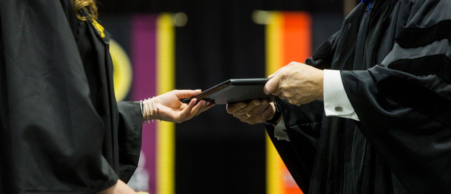 person in a black gown handing a diploma to a student in a black gown